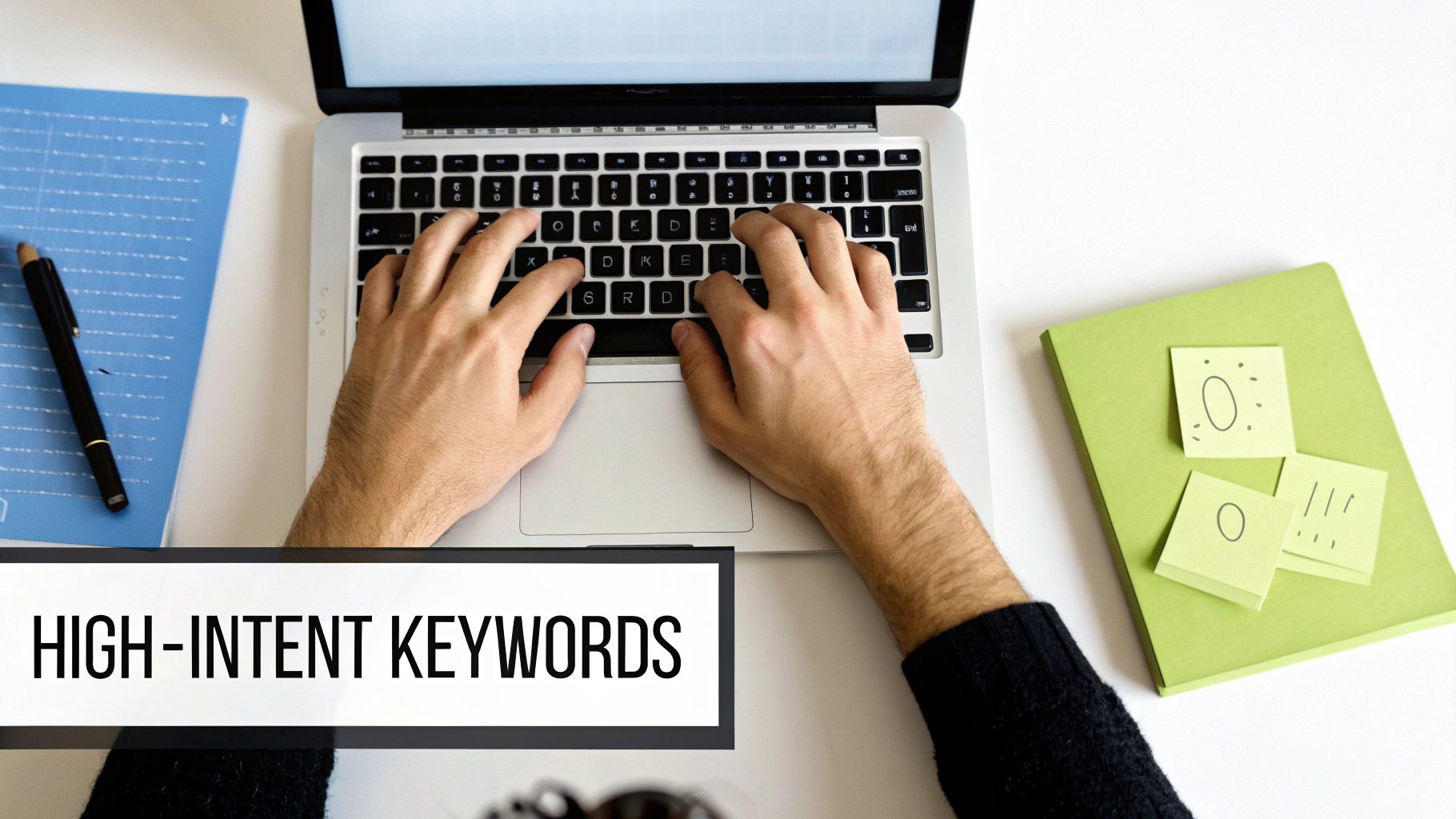 Overhead view of hands typing on a laptop, surrounded by notebooks and a banner stating 'HIGH-INTENT KEYWORDS'.